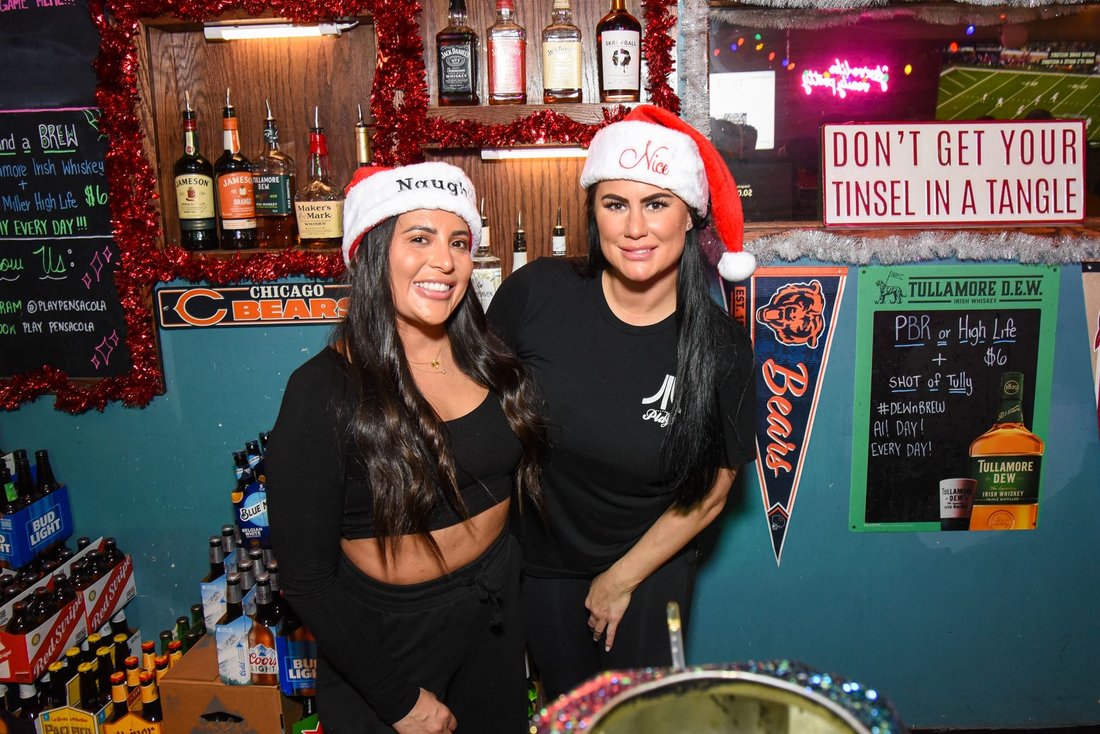 Two Play Pensacola bartenders in Santa hats behind the bar